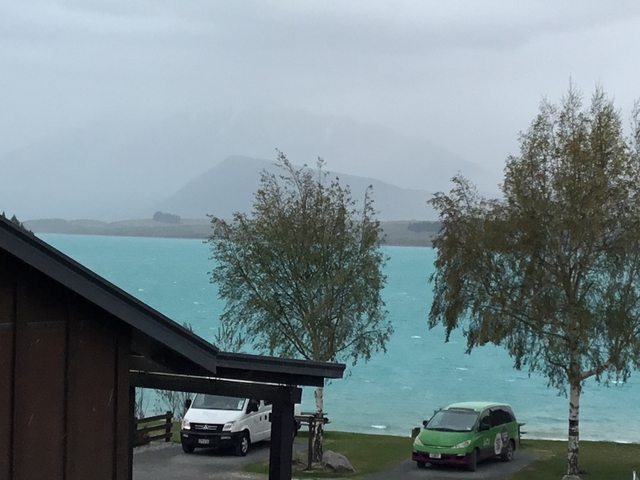       A turquoise lake with trees and mountains in misty weather.
  
