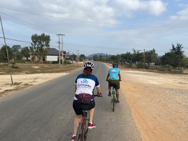 Two cyclists on a rural road with clear skies.