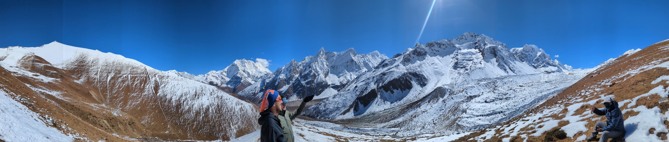 People admiring the view of snowy peaks on a sunny day.