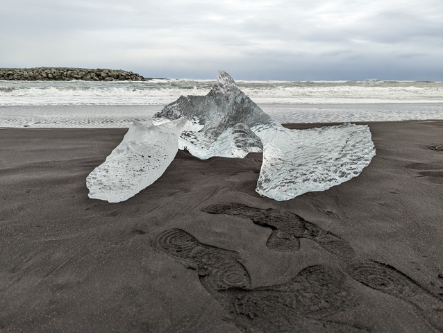 Ice on black sand beach with ocean waves in the background.