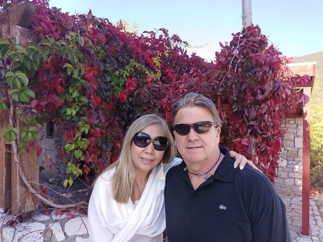 A couple posing with red autumn leaves on a wall.