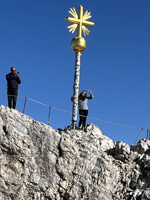 Person posing at a mountain peak with cross.