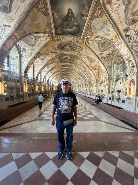 Person standing in a hall with ornate ceiling and mirrored walls.