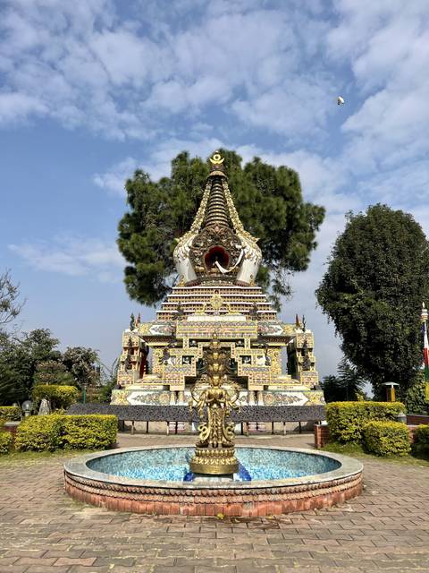       An elaborately decorated stupa with green foliage around.
  