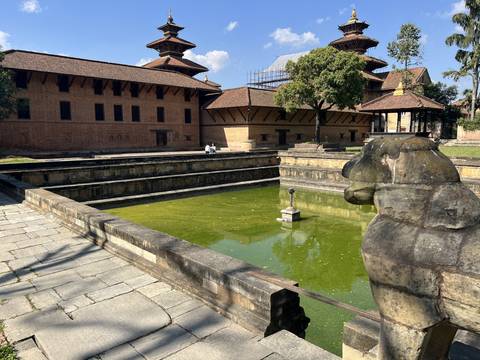       A large stone courtyard with a central pool and buildings.
  