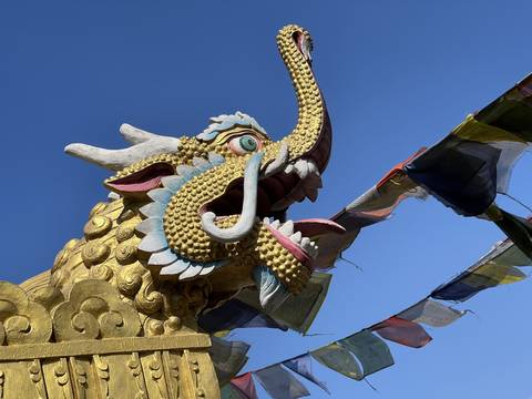       A decorative dragon head with prayer flags under a blue sky.
  