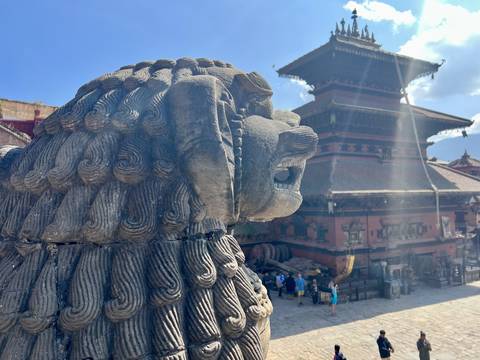       A stone lion statue overlooking a temple square with people.
  