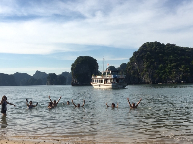 People swimming near a boat with limestone karsts in the background.