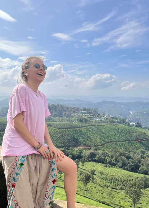 Woman smiling with a tea plantation landscape in the background.