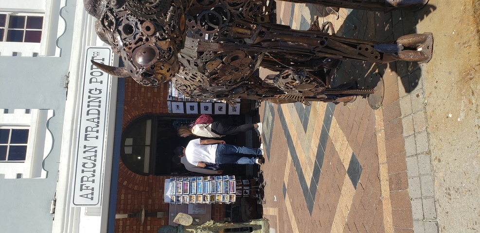 People walking past a shop with a large sculptural art piece.