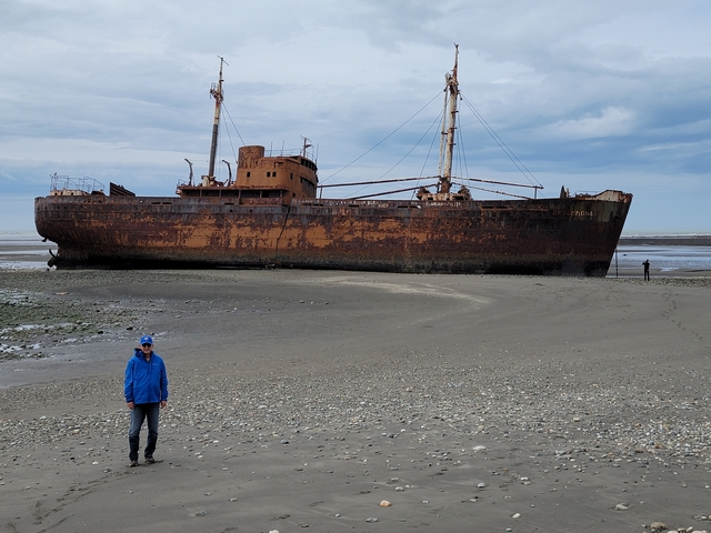       Man walking on a beach near an old shipwreck.
  