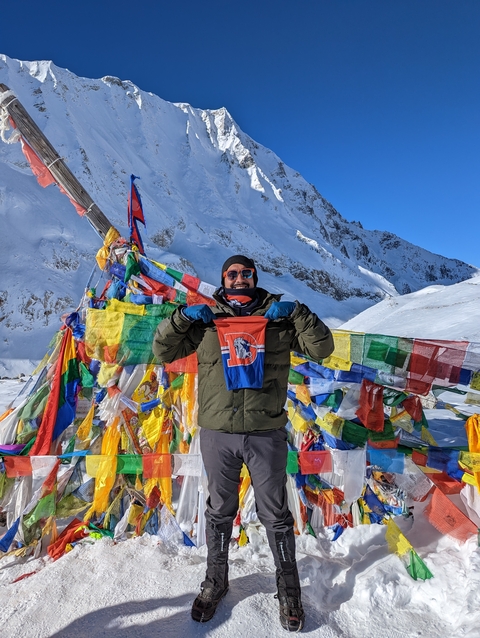 Person holding a flag in a snowy mountainous landscape with prayer flags.