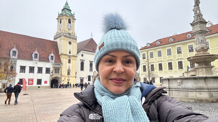       Person posing in a city square with historical buildings.
  