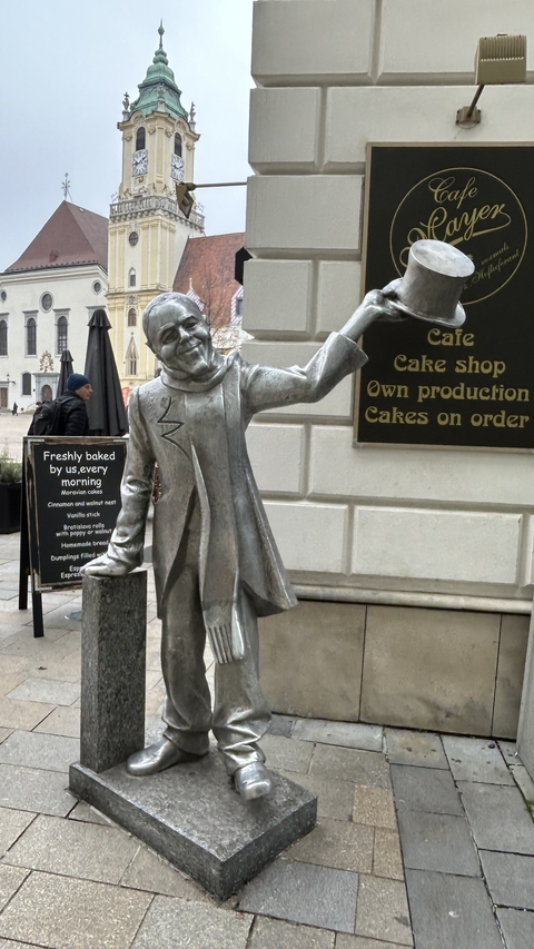       Statue of a man near a cafe sign.
  