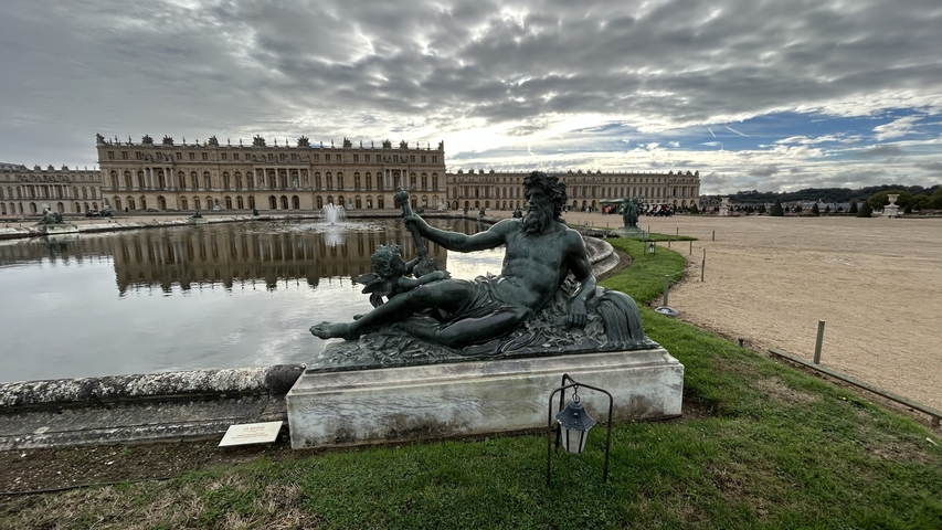 Statue in front of a large chateau and reflection pool.