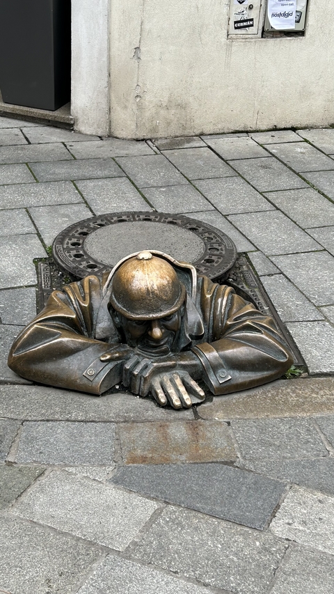       Statue of a man emerging from a sewer.
  