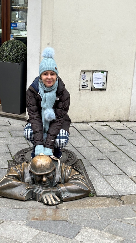       Person crouching near a statue on a sidewalk.
  