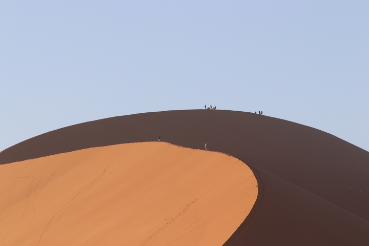 People walking on a large, arid sand dune.