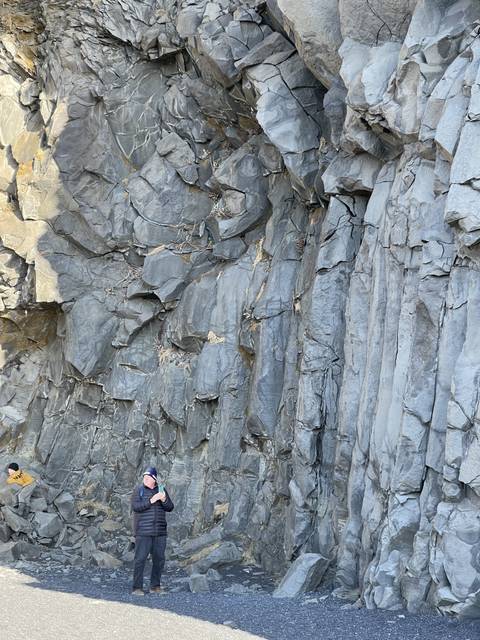 Person standing in front of a basalt column rock formation.