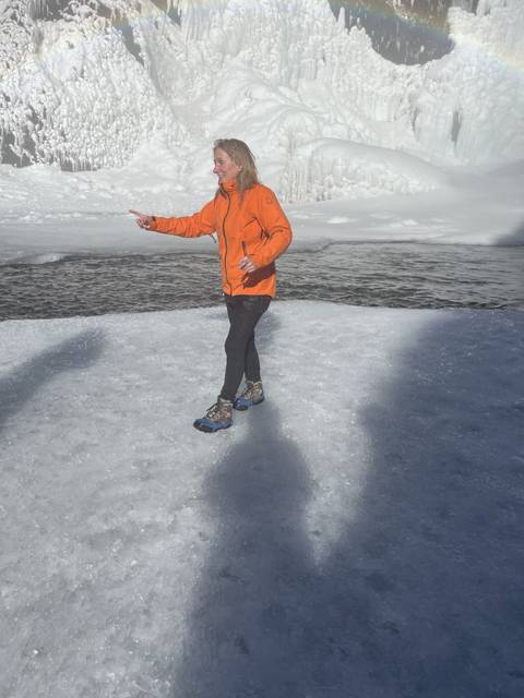 Person standing on icy ground with a frozen waterfall nearby.
