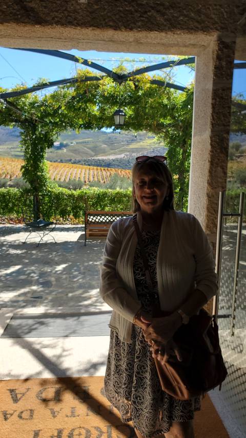 Person standing by a vineyard with hills in the background.