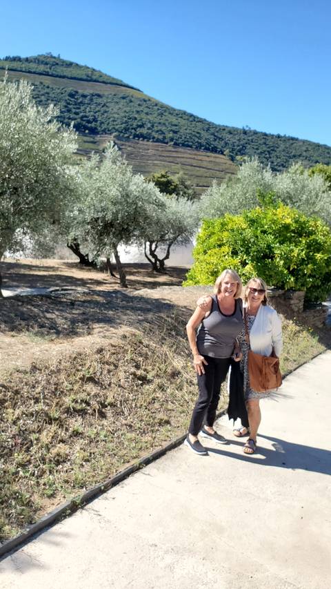 Two people standing in a vineyard area with a scenic background.