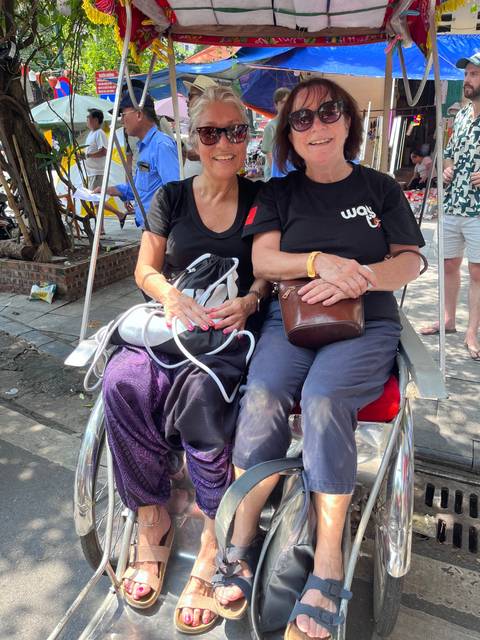       Two people sitting in a rickshaw, posing for the photo with smiles.
  