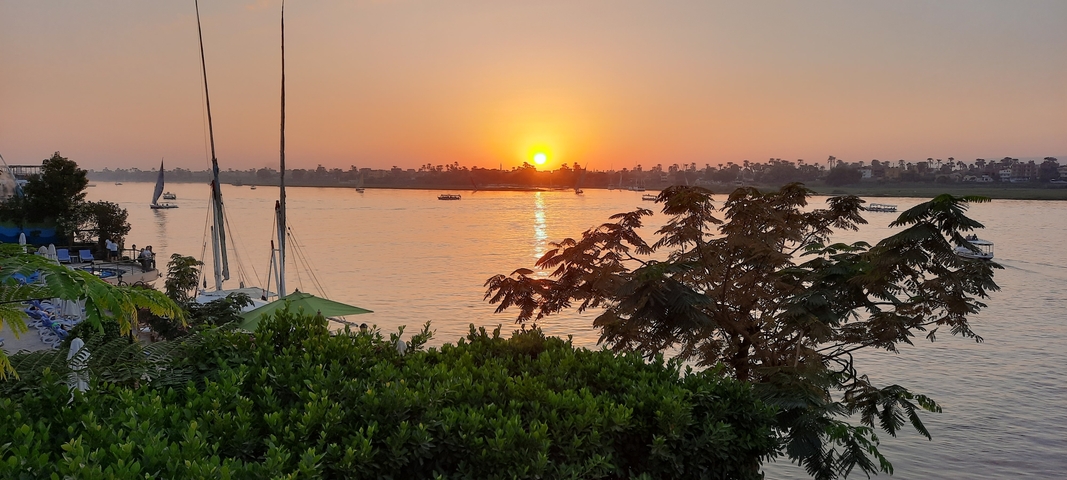 Sun setting over a river with boats anchored.