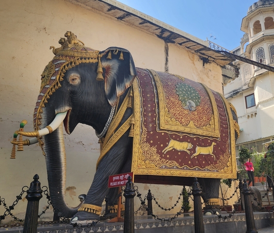       Ornate elephant mural on a wall with people nearby.
  
