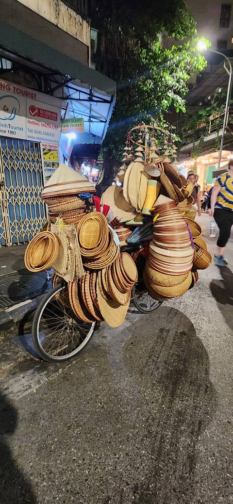 Bicycles piled with hats on a street at night.