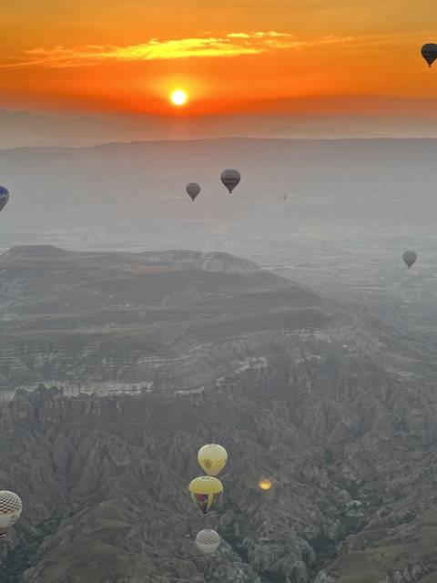       Hot air balloons at sunrise in a mountainous area.
  
