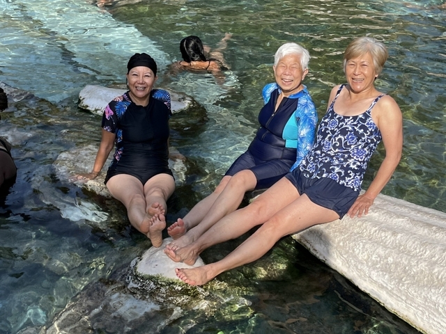       Three women sitting on white rocks in a pool of water, enjoying a relaxing moment.
  