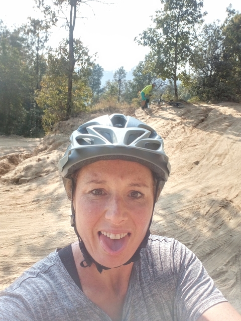 Woman in a helmet posing on a dirt path with a bicycle.