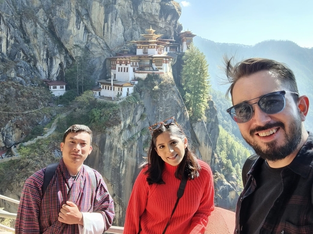       Three people smiling in front of the Tiger's Nest Monastery.
  