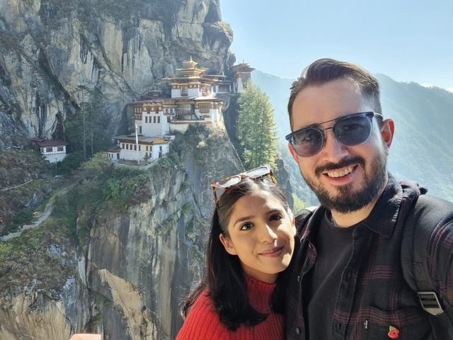       Two people posing with the Tiger's Nest Monastery in the background.
  