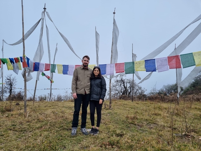      Couple posing in front of prayer flags in a natural setting.
  