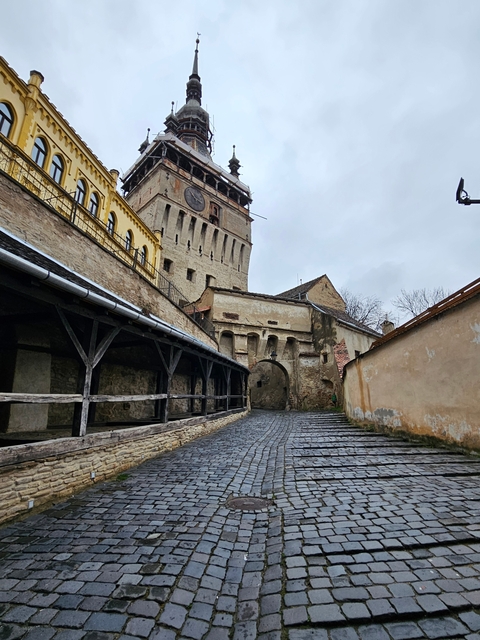       Clock tower and cobblestone street in a historical setting.
  