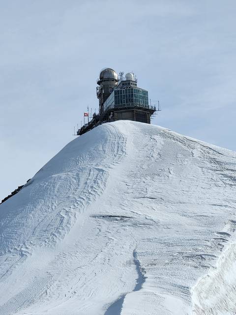 Snow-covered mountain observatory with Swiss flag.