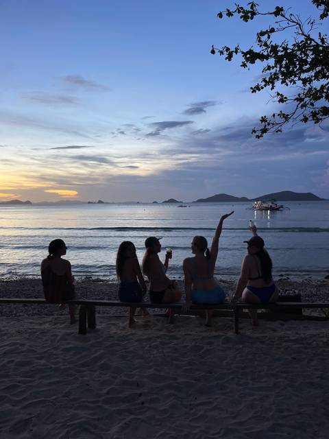       People sitting on a beach looking out over the sea at sunset.
  