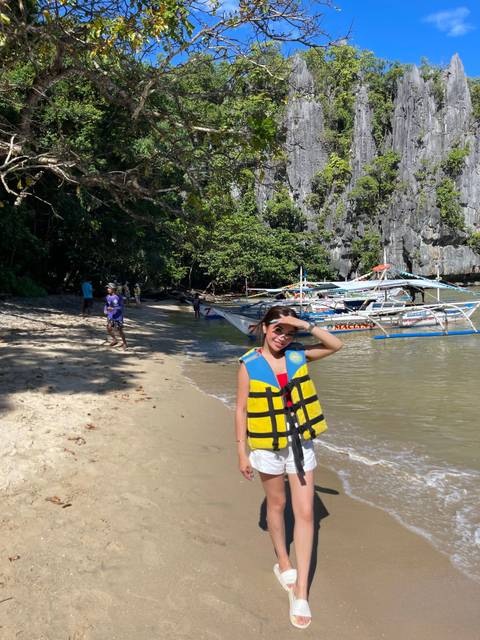 Person standing on a beach wearing a life jacket and hat.