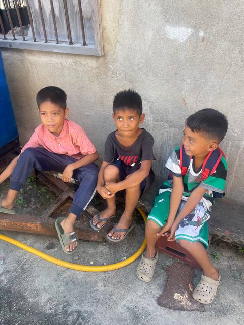 Three children sitting on a sidewalk outdoors.