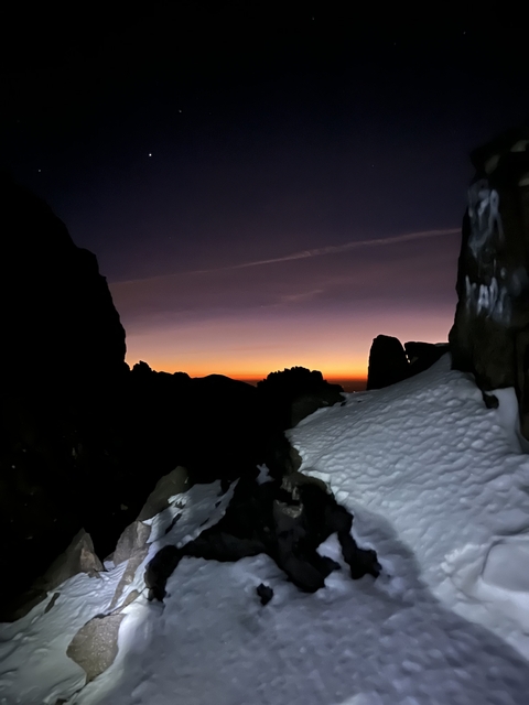 Snowy mountain landscape during twilight with a narrow passage between rocks.