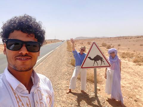       Two people in front of a camel crossing sign in the desert.
  