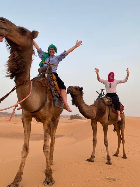       Two people joyously riding camels in the desert.
  