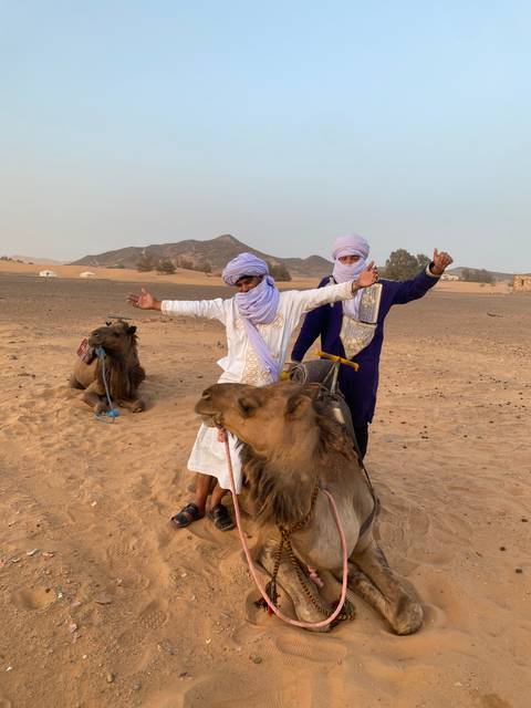       Two people with camels in a desert setting.
  