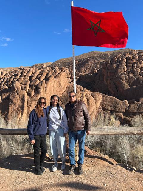       People posing near a flag with rocky backdrop.
  