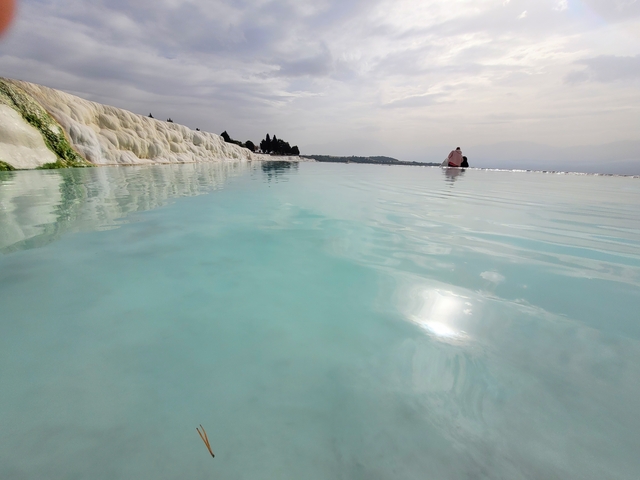       A turquoise pool with white limestone terraces.
  