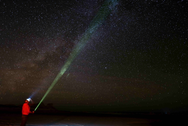       Person with a green laser pointer under a starry sky.
  