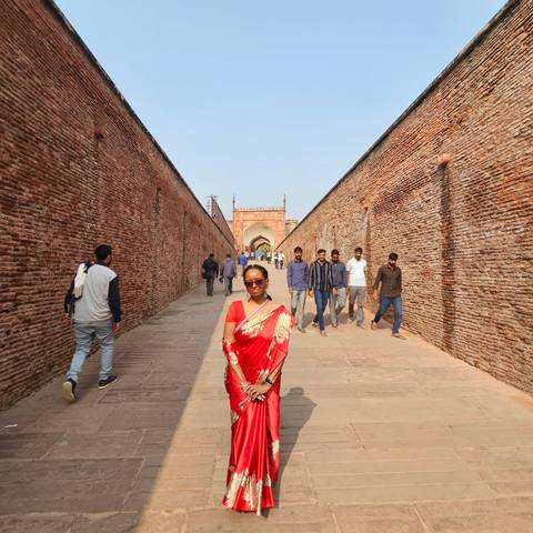 Woman in red sari with sunglasses in a historic site.