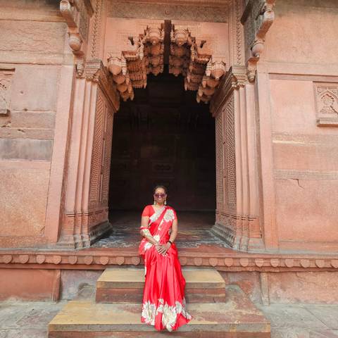 Woman posing in a red sari at a historic entrance.